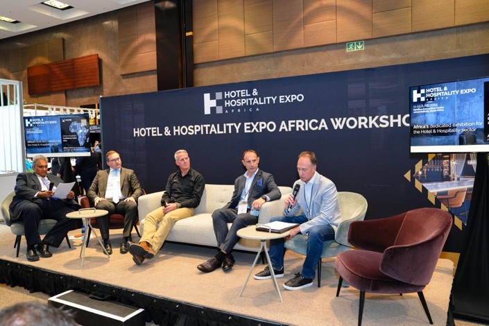 Panel discussion at Hotel & Hospitality Expo Africa Workshop with five individuals seated on stage and event branding backdrop.