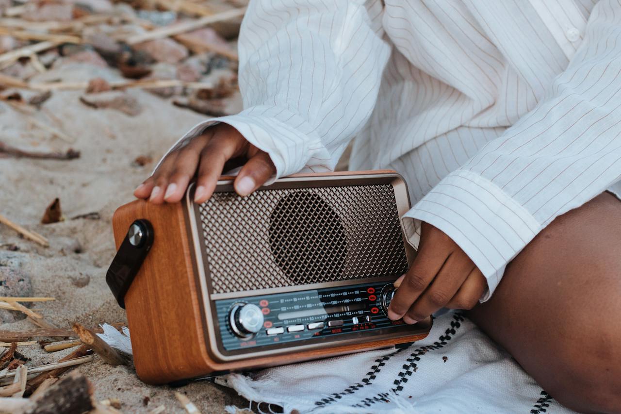 Services 8 Individual seated on sandy surface adjusting vintage wooden radio with pinstriped shirt.