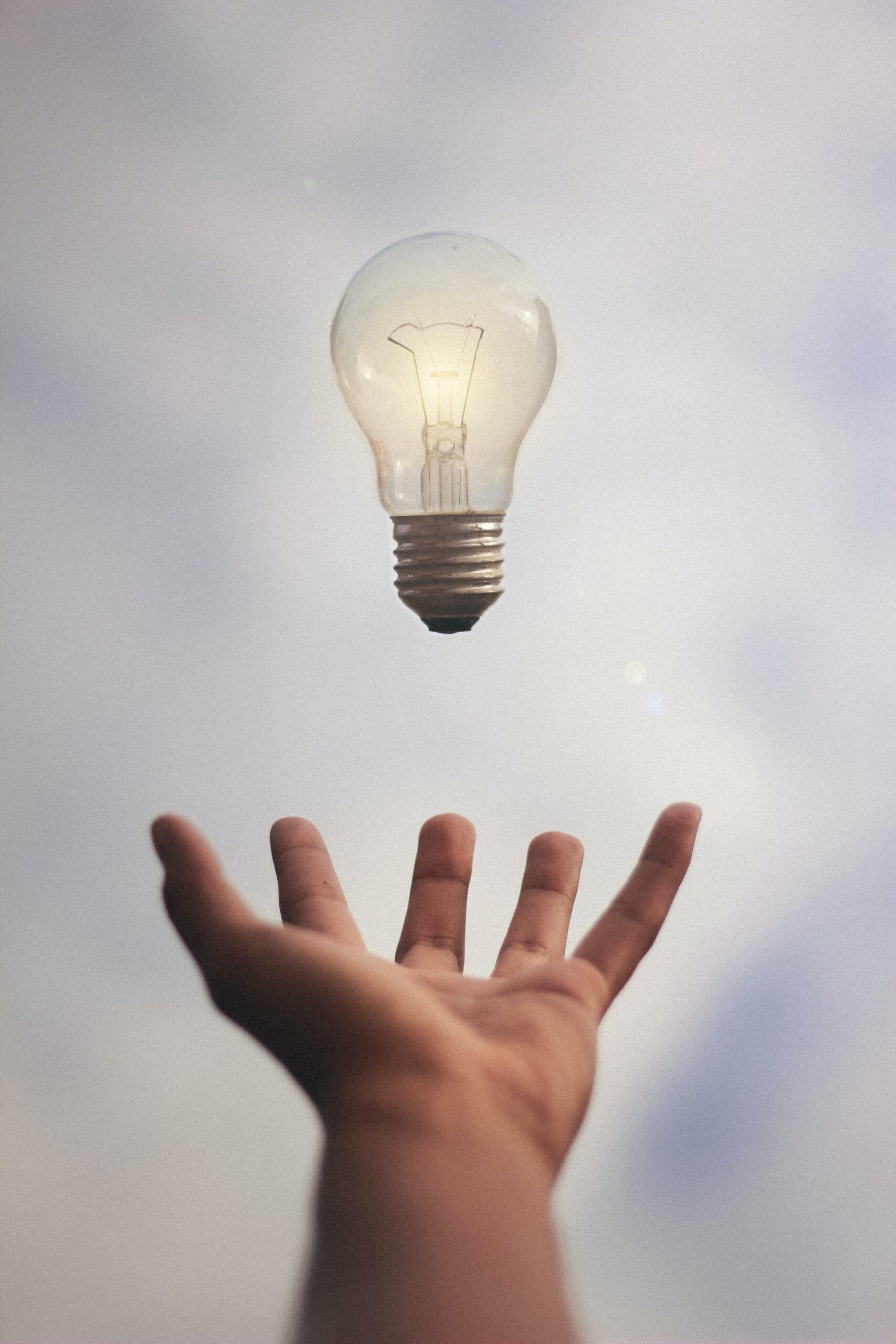Services 1 Hand reaching toward a floating light bulb against a soft sky. Pulse Communication | Services