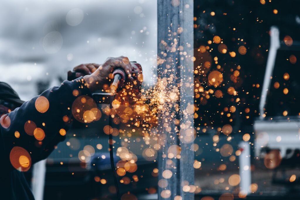 Close-up of person using angle grinder on vertical metal surface with bright orange sparks flying outward.