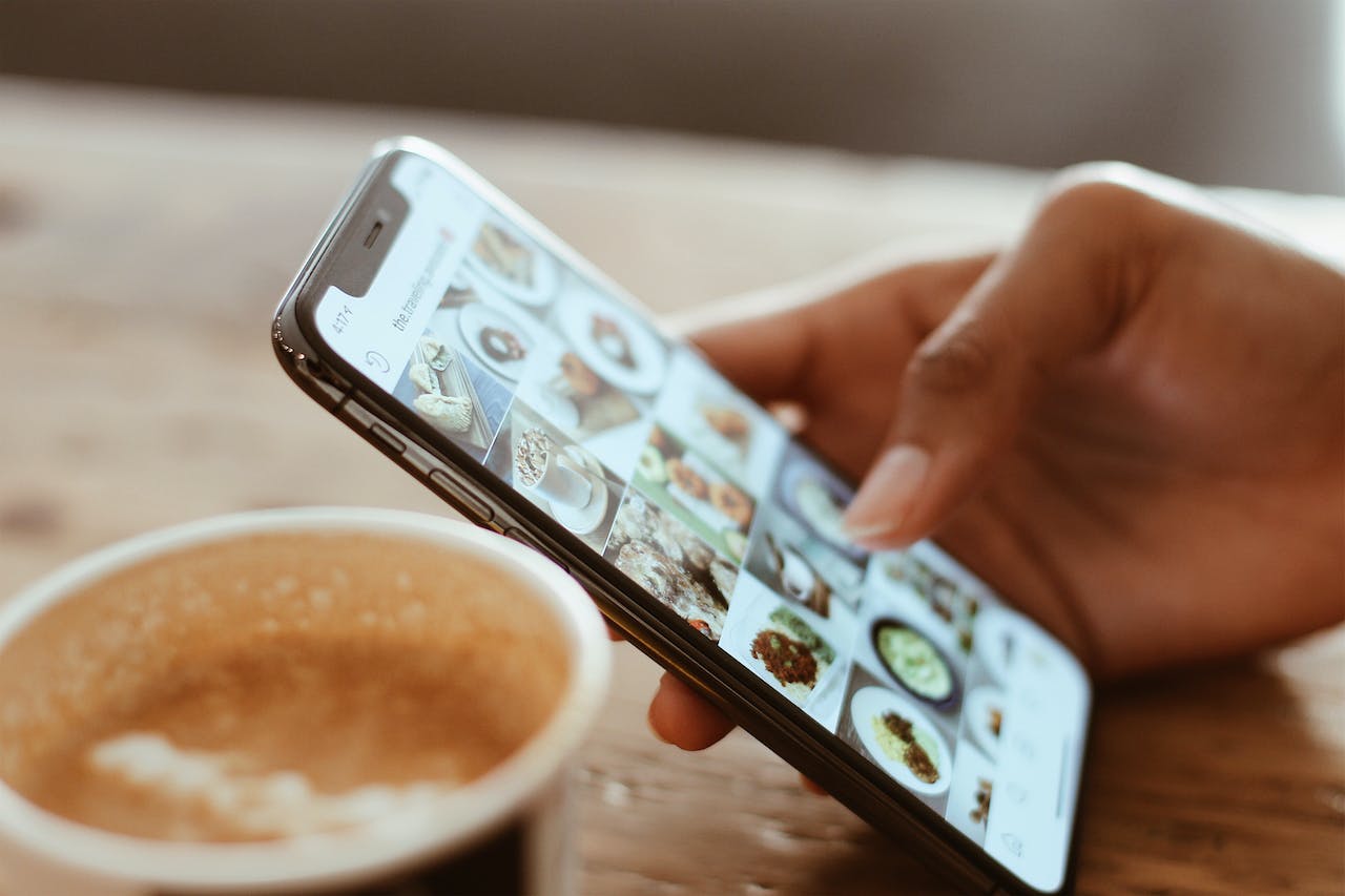 Services 9 Individual browsing food photographs on a smartphone with a cup of coffee.